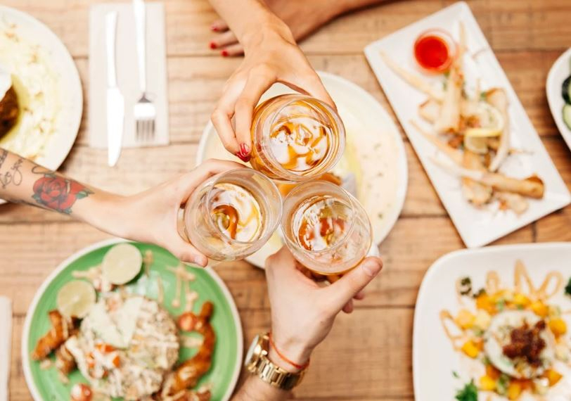 Hands clicking glasses over a table of appetizers